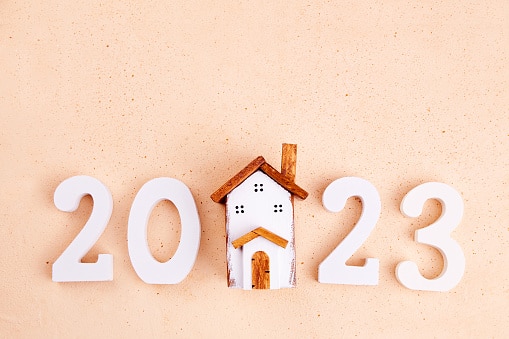 Happy New Year 2023 and Merry Christmas greeting card. A toy wooden house and white numbers 2023 on a light background. Copy space, top view.